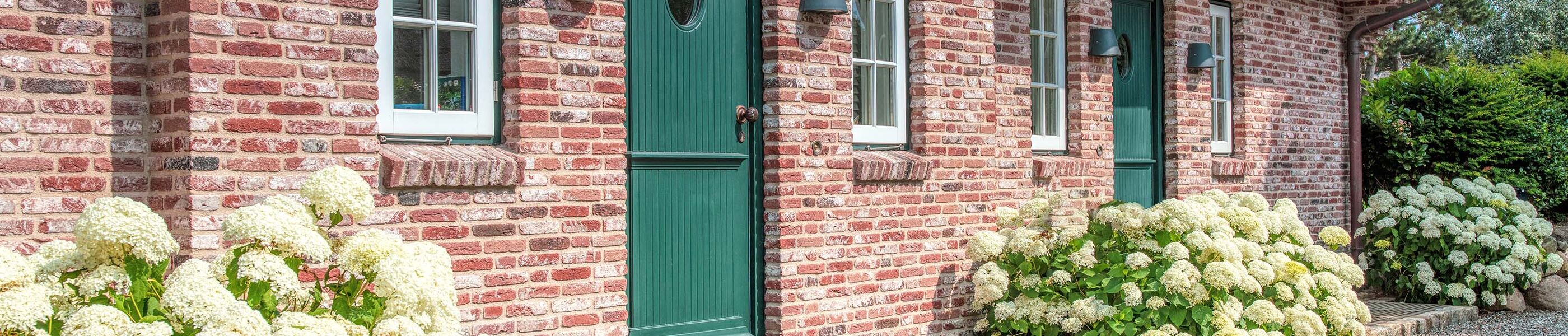 Backsteinhaus auf Sylt mit grüner Tür, Fenstern und Hortensien vor der Fassade