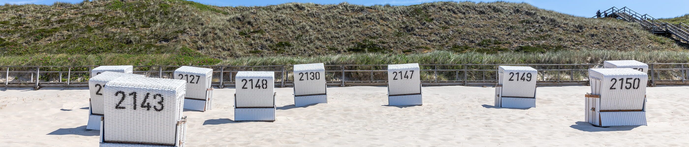 Strandkörbe auf Sylt mit Nummern im Sand vor Dünenlandschaft